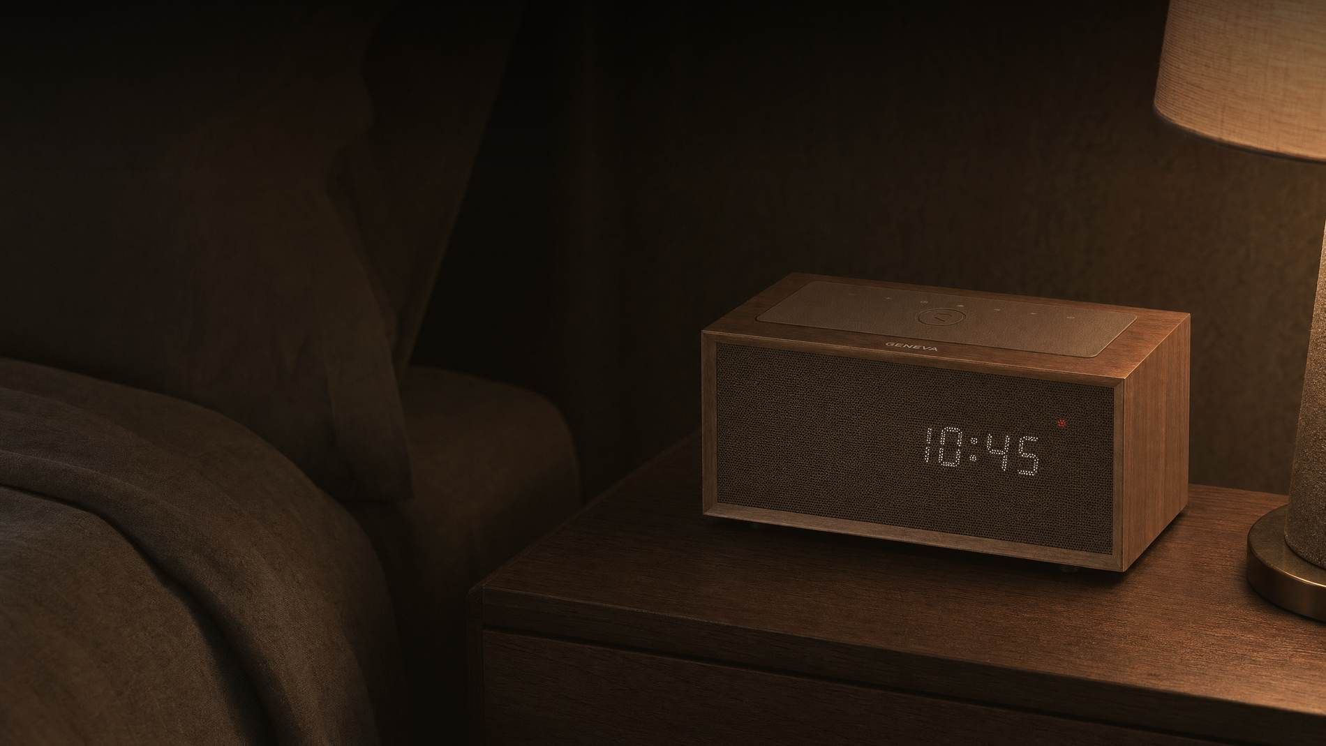 A Geneva Time digital clock radio in walnut on a nightstand beside a bed in a hotel room at night