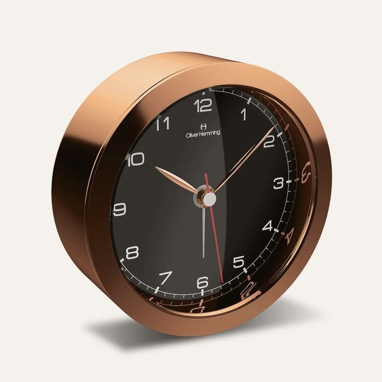 An Oliver Hemming Desire clock in rose gold with a black dial, also shown in gold with a white dial