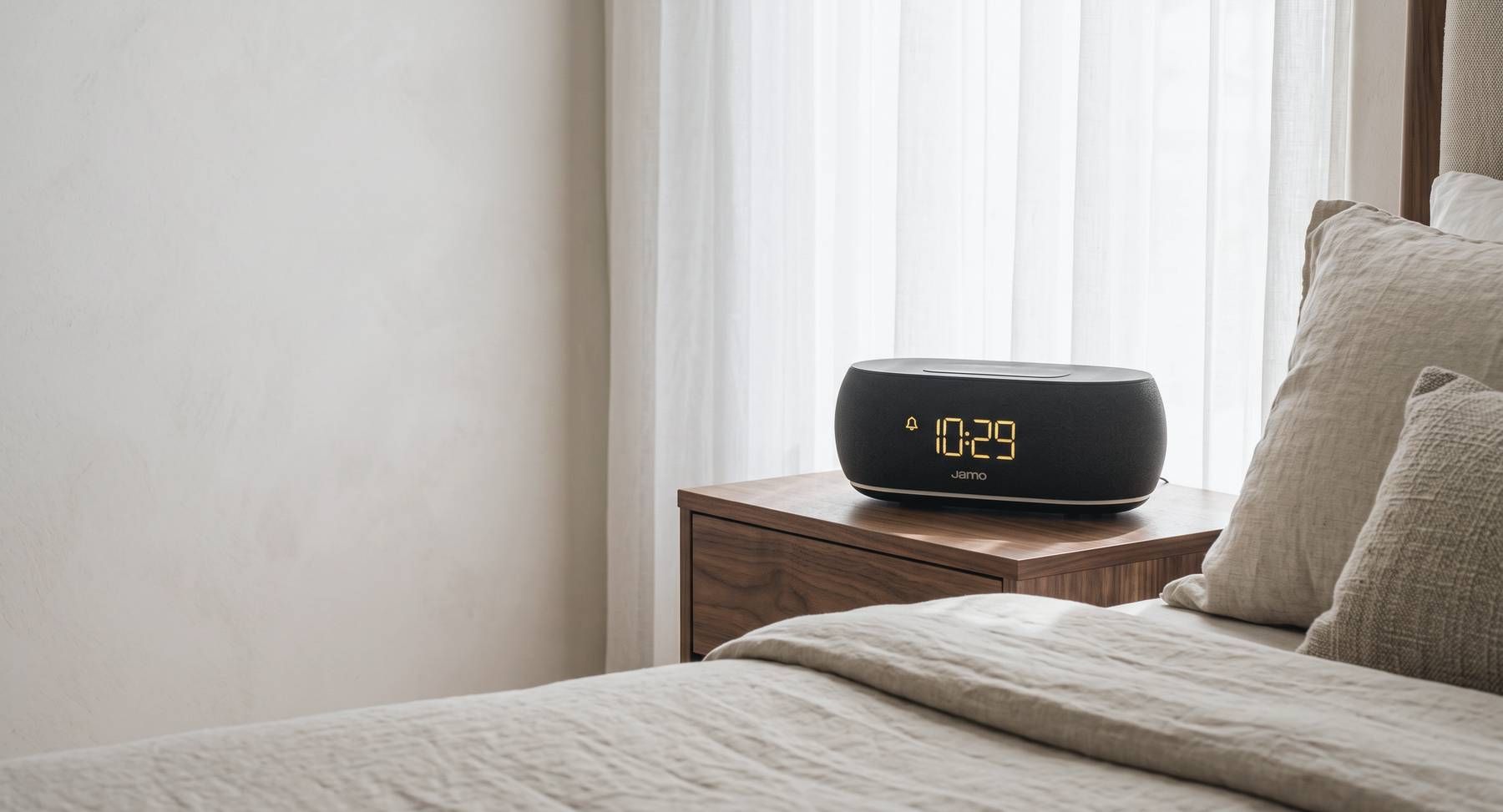 A Jamo HYG Reflect on a nightstand beside a bed in a daylit guest room