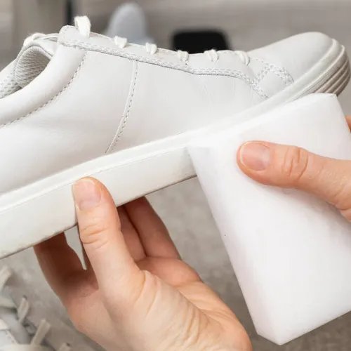 ผู้หญิงกำลังใช้ฟองน้ำทำความสะอาดพื้นรองเท้าผ้าใบสีขาว ซึ่งเป็นขั้นตอนสำคัญในวิธีซักรองเท้าผ้าใบสีขาว