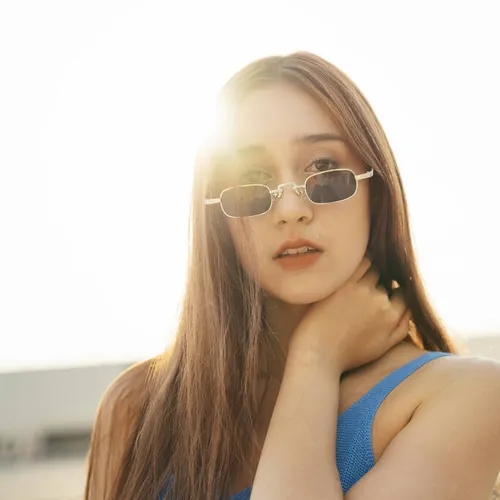 หญิงสาวผมยาวสวมแว่นกันแดด มองตรงมาที่กล้อง แสงแดดส่องจากด้านหลัง ภาพถ่ายแบบแสงย้อน