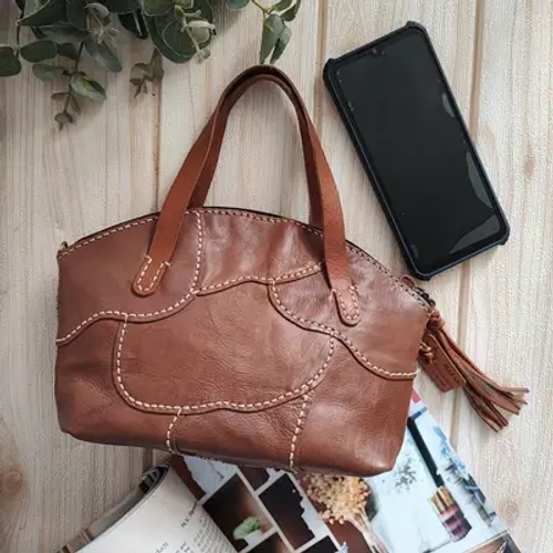 กระเป๋าหนังเสียทรงวางอยู่บนพื้นไม้