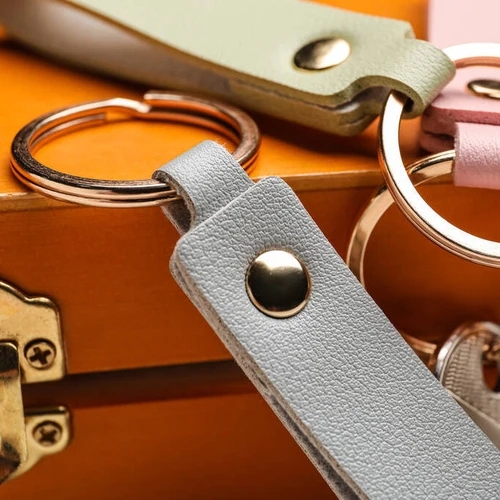 พวงกุญแจหนังสังเคราะห์สีพาสเทล 3 ชิ้น พร้อมห่วงโลหะสีทองวางซ้อนกันบนกล่องไม้สีส้ม