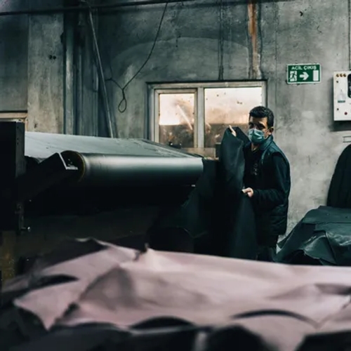 คนงานในโรงฟอกหนังกำลังจัดการแผ่นหนังสีดำขนาดใหญ่ด้วยเครื่องจักรสายพาน