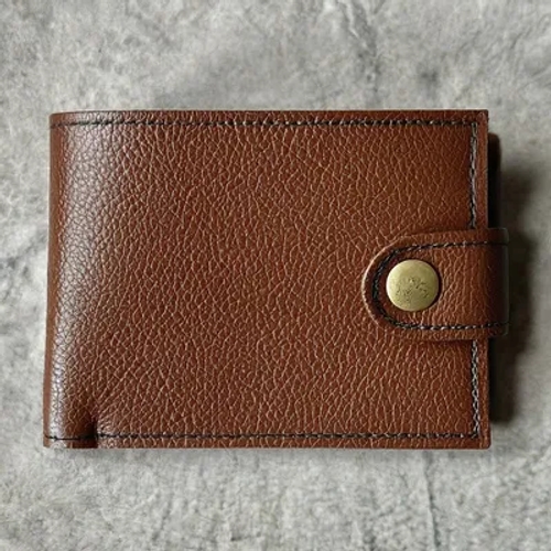 กระเป๋าสตางค์ผู้ชายสีน้ำตาลทำจากหนังเทียม ผิวสัมผัสแบบมีเกรน มีกระดุมแป๊กปิดอยู่บนพื้นผิวสีเทา