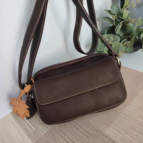 กระเป๋าสะพายข้างหนังแท้สีน้ำตาลเข้ม ทรงกะทัดรัด มีสายสะพายยาวและพวงกุญแจหนังประดับ