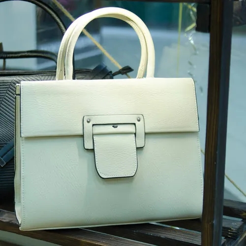 กระเป๋าถือสีครีมดีไซน์หรูหราวางบนชั้น