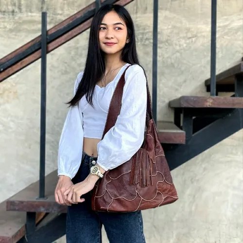 ผู้หญิงสะพายกระเป๋าหนังสีน้ำตาลเข้ากับลุคลำลอง
