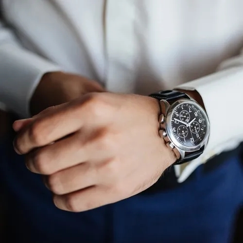 ผู้ชายสวมนาฬิกาข้อมือตัวเรือนเงินสายหนังสีดำ ใส่คู่กับเสื้อเชิ้ตสีขาว