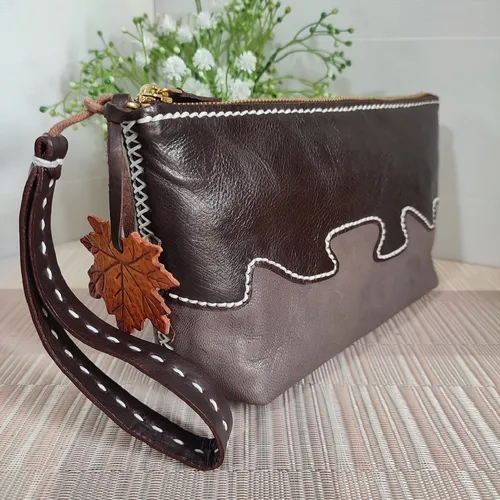 กระเป๋าคลัทช์หนังสีน้ำตาลเข้มและเทา พร้อมสายคล้องข้อมือและจี้ใบเมเปิล ตะเข็บสีขาวละเอียด