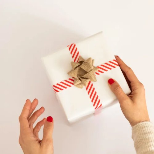 ผู้หญิงกำลังยื่นกล่องของขวัญสีขาวผูกโบว์ให้