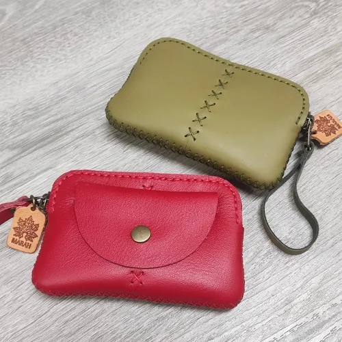 กระเป๋าหนังเย็บมือสองใบ สีแดงและสีเขียวมะกอก วางอยู่บนพื้นไม้