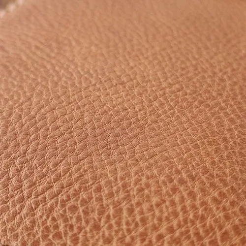 ภาพระยะใกล้ของพื้นผิวหนังสีน้ำตาลอ่อนมีลายหนังธรรมชาติ ซึ่งแสดงให้เห็นถึงรายละเอียดของพื้นผิววัสดุ