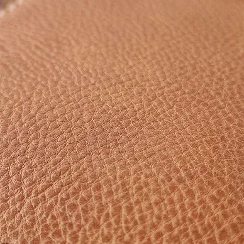 ภาพระยะใกล้ของพื้นผิวหนังสีน้ำตาลอ่อนมีลายหนังธรรมชาติ ซึ่งแสดงให้เห็นถึงรายละเอียดของพื้นผิววัสดุ