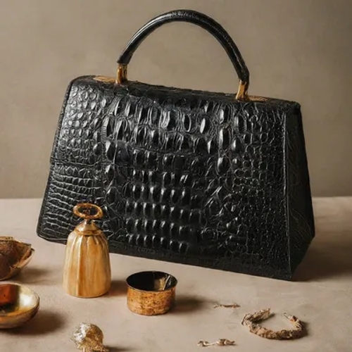 กระเป๋าถือหนังจระเข้สีดำเงา ตั้งอยู่บนพื้นผิวสีอ่อน ล้อมรอบด้วยของตกแต่งสีทองและทองเหลือง
