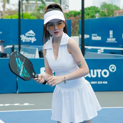 ผู้หญิงสวมชุดกีฬาเทนนิสสีขาว หมวกไวเซอร์ แว่นกันแดด ถือไม้พายบนคอร์ทสีฟ้า