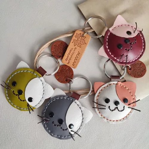 พวงกุญแจหนังรูปหน้าแมวสีต่างๆ มีหูและหนวด พร้อมป้ายไม้แกะสลักและจี้รูปใบไม้