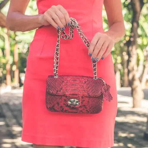 ผู้หญิงในชุดเดรสสีส้มคอรัลถือกระเป๋าสะพายข้างหนังงูสีแดงเข้ม
