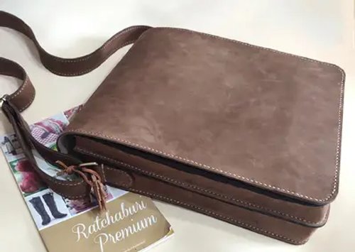 กระเป๋าสะพายหนังแท้สีน้ำตาลเข้มวางบนพื้นผิวสีอ่อนพร้อมเอกสาร แสดงถึงความเป็นทางการและความน่าเชื่อถือ
