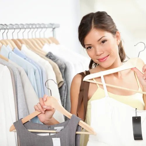ผู้หญิงกำลังถือเสื้อผ้าสองชุดบนไม้แขวนเสื้อ โดยมีเสื้อผ้าแขวนอยู่บนราวเสื้อด้านหลัง