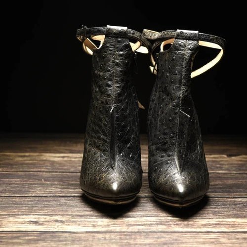 รองเท้าบูทส้นสูงหนังนกกระจอกเทศสีดำ สายรัดข้อเท้าและปลายแหลม วางบนพื้นไม้เข้ม