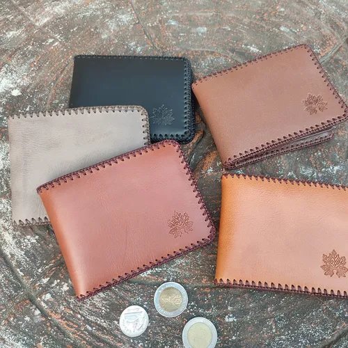 กระเป๋าสตางค์หนังแฮนด์เมด 5 ใบหลากสีดำ เทา น้ำตาล วางเรียงบนพื้นหิน มีเหรียญวางข้างๆ