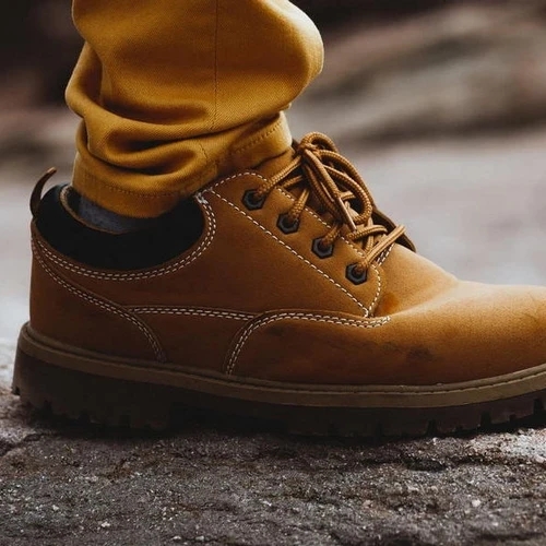 รองเท้าบูทหนังสีน้ำตาลอ่อน สวมคู่กับกางเกงสีเหลืองมัสตาร์ด ยืนอยู่บนพื้นคอนกรีต