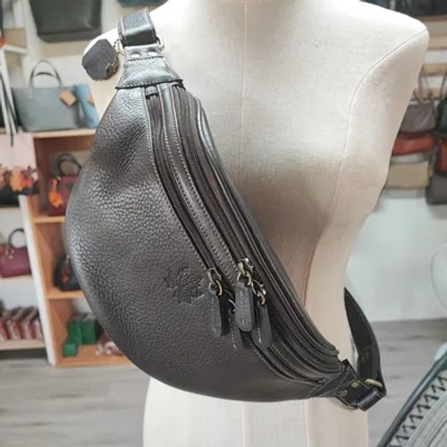 กระเป๋าคาดอกหนังแท้สีน้ำตาลเข้มลายเม็ดหนังวางอยู่บนหุ่นโชว์ มีซิปหลายช่องและโลโก้รูปใบไม้