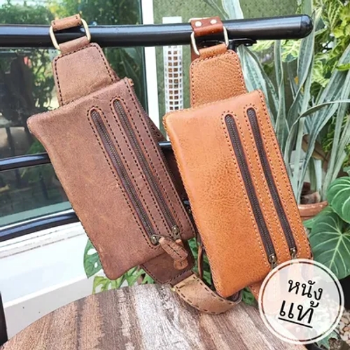 กระเป๋าคาดอกหนังแท้สองใบ สีน้ำตาลเข้มและสีแทนอ่อน แขวนอยู่บนราวเหล็กสีดำ โดยมีข้อความ 'หนังแท้' กำกับที่ใบสีแทน