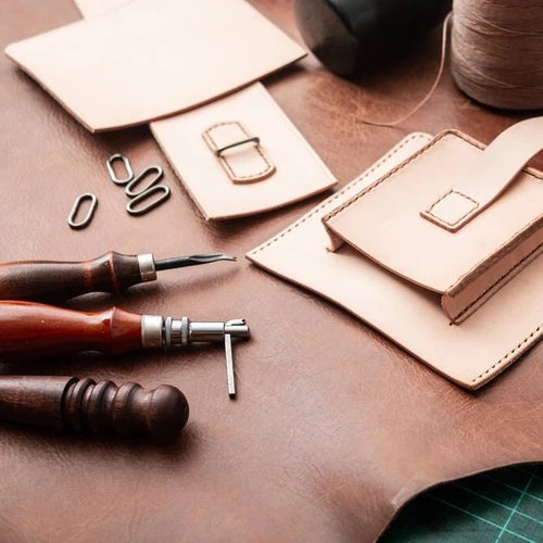 อุปกรณ์สำหรับงานเครื่องหนังและชิ้นส่วนหนังวัวสีอ่อนที่กำลังถูกประดิษฐ์ วางอยู่บนพื้นหนังสีน้ำตาลเข้ม
