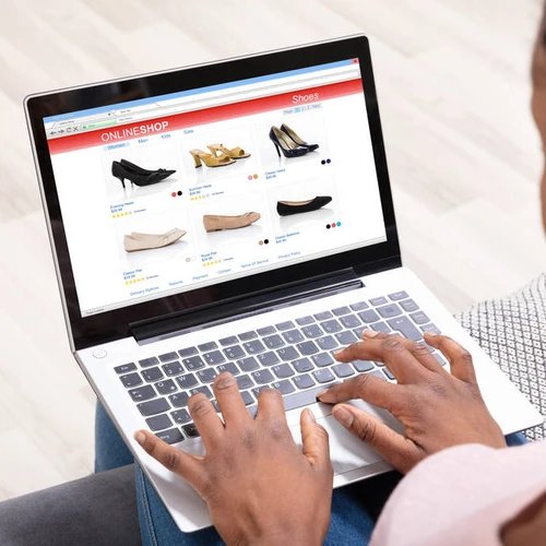ผู้หญิงกำลังเลือกซื้อรองเท้าในร้านค้าออนไลน์ผ่านแล็ปท็อป โดยมีมือวางอยู่บนแป้นพิมพ์