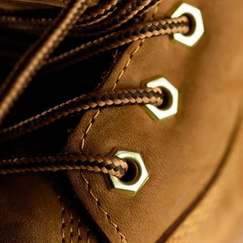 ภาพระยะใกล้ของรองเท้าบูทหนังนูบัคสีน้ำตาล แสดงพื้นผิวละเอียดของหนัง เชือกรองเท้า และตาไก่หกเหลี่ยมสีทอง