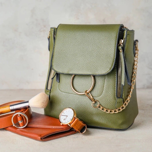 กระเป๋าสะพายสีเขียวมะกอกหนังลาย ประดับอะไหล่วงแหวนสีทอง วางคู่กับกระเป๋าสตางค์และนาฬิกา