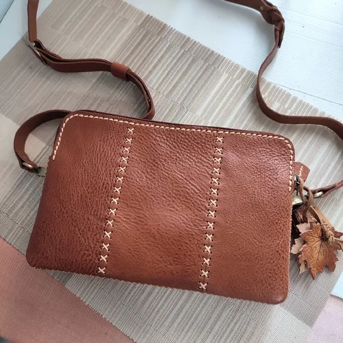 กระเป๋าสะพายข้างหนังแท้สีน้ำตาลที่ตกแต่งด้วยลายเย็บและพวงกุญแจ เพิ่มความน่าสนใจ