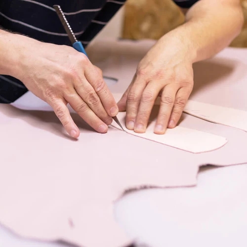 ช่างกำลังใช้มีดตัดแผ่นหนังควายตามรูปทรงของแม่พิมพ์อย่างประณีตบนโต๊ะทำงาน