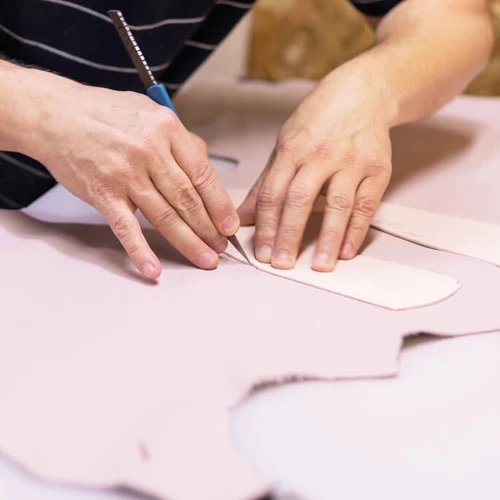 ช่างกำลังใช้มีดตัดแผ่นหนังควายตามรูปทรงของแม่พิมพ์อย่างประณีตบนโต๊ะทำงาน