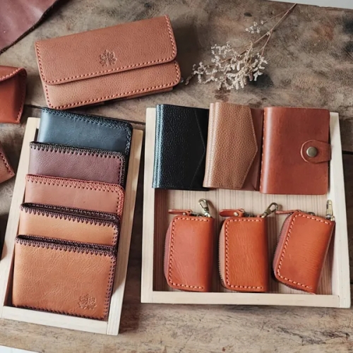 กระเป๋าสตางค์และเคสหนังหลากหลายดีไซน์และสีสัน จัดวางเรียงในถาดไม้บนพื้นโต๊ะไม้