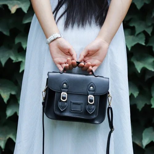 ผู้หญิงสวมชุดเดรสลายทางสีอ่อน ถือกระเป๋าสะพายข้างสีดำใบเล็กดีไซน์คลาสสิกพร้อมหัวเข็มขัดสีทอง