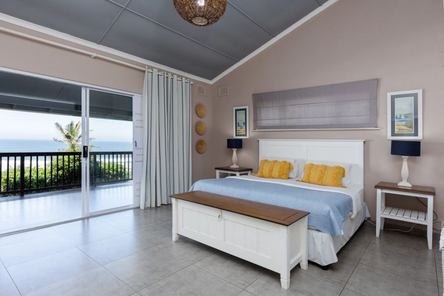 Bedroom with ocean views through sliding doors, a blue and white colour scheme, and mustard yellow accent pillows on the bed.