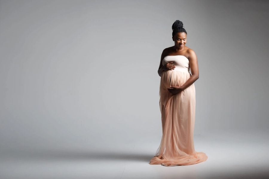 Expectant mother in a flowing blush tulle gown, cradling her bump in soft studio light at Studio 039, Sea Park.