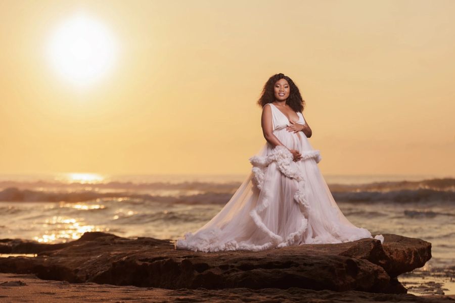 Expectant mother in a full blush tulle gown on a rock at the water’s edge, the sun rising over the sea, St Michael’s.