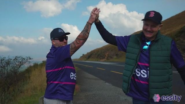 Two Essity team members in branded shirts giving a high five beside a mountain road near Hoedspruit