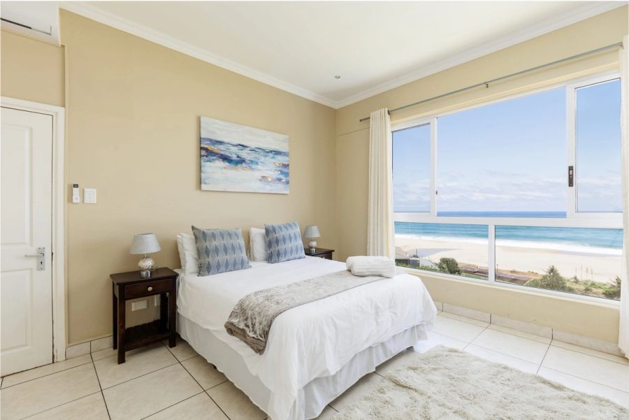 Guest bedroom with a double bed and a large window overlooking the beach and ocean at Colonial Sands, Margate