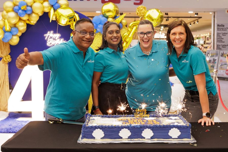 Shelly Centre staff in teal shirts celebrating around a sparkler-lit cake at the centre’s 40th birthday, Shelly Beach.
