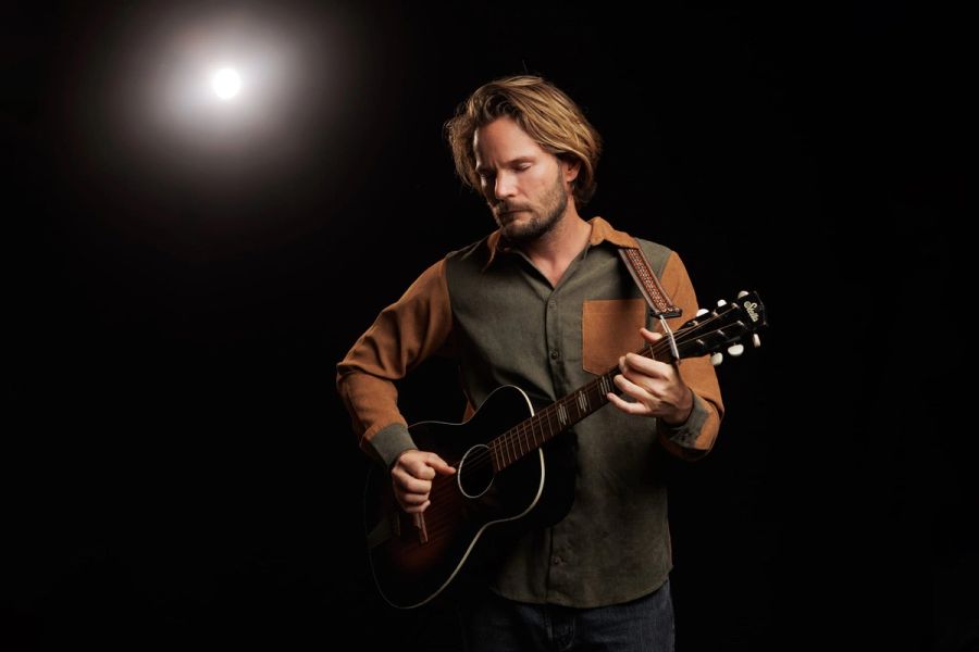Musician Tyran Roy playing an acoustic guitar under a single spotlight against a black background, photographed for his album cover.