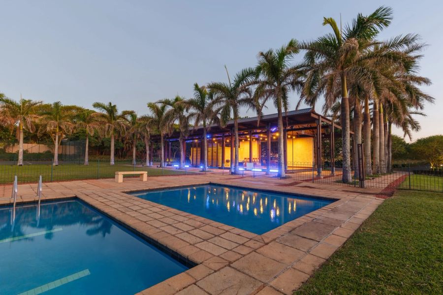 Estate swimming pool at dusk with a glowing palm-lined pavilion reflected in the water, Zinkwazi