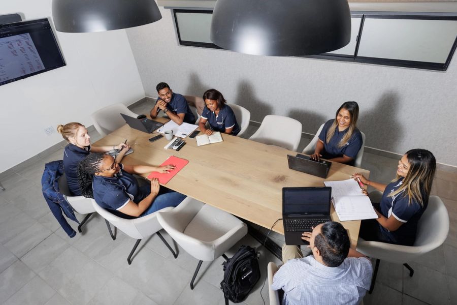 Business team in navy uniforms meeting around a boardroom table with laptops, photographed from above, Port Shepstone.