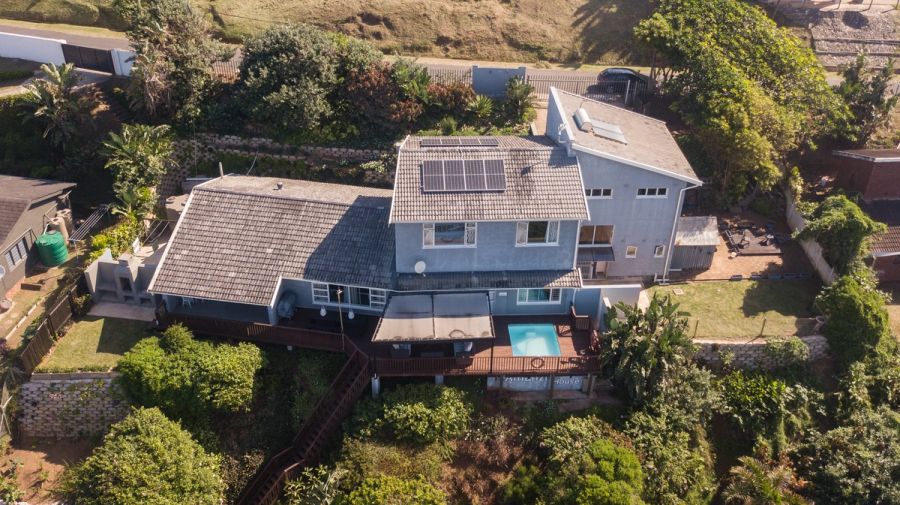 Aerial view of a double-storey coastal home with solar panels, a wooden deck, swimming pool, and lush garden surrounds.