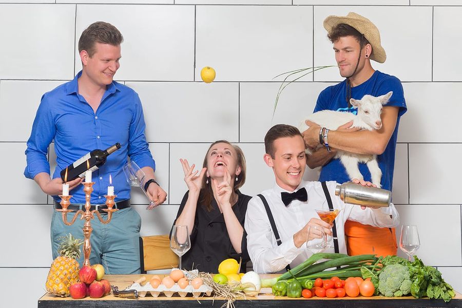 Playful restaurant team photo: four staff with wine, a cocktail shaker, a baby goat and fresh produce against a white tiled wall, Margate