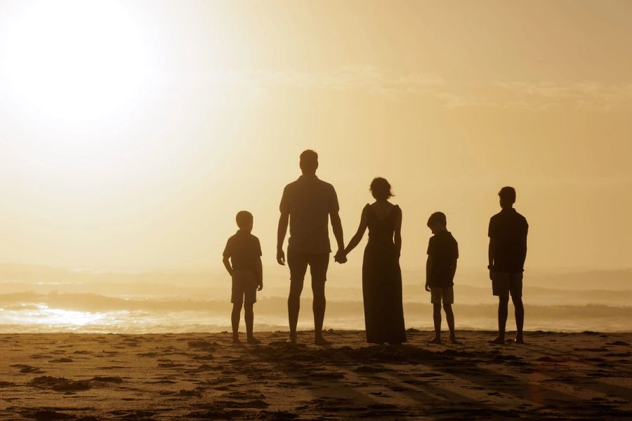 Family of five holding hands in silhouette, facing the sea at sunrise on Margate beach.